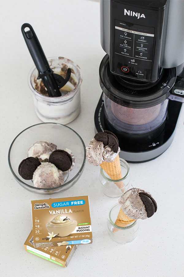 Top view of Ninja Creami, scooped pudding ice cream, and Simply Desserts vanilla pudding box on a white countertop