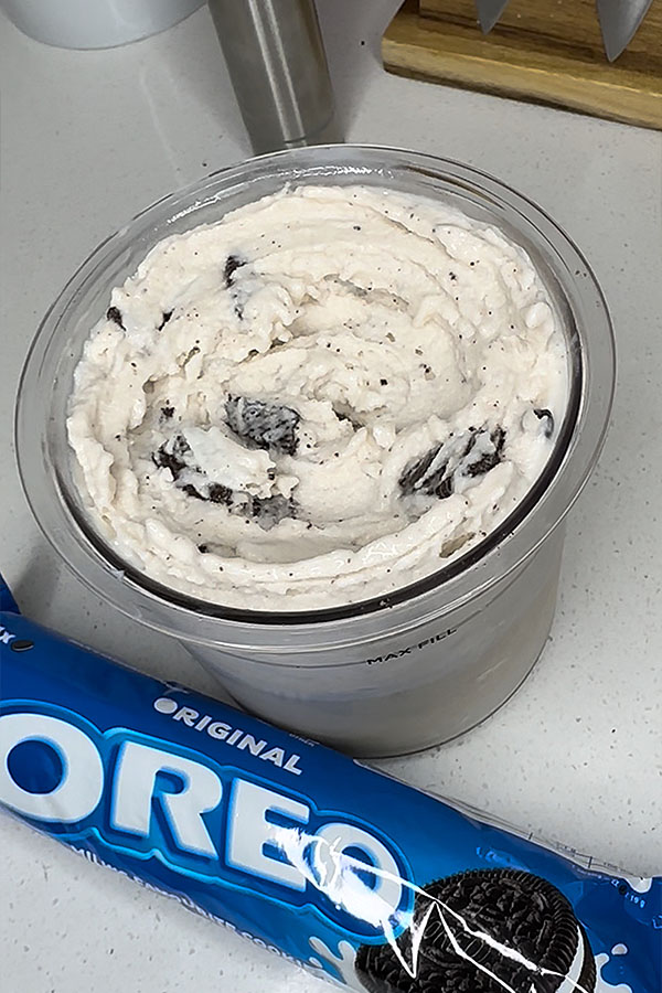 A close-up of a creamy Oreo protein ice cream inside a Ninja Creami container, with visible cookie chunks and an Oreo packet beside it