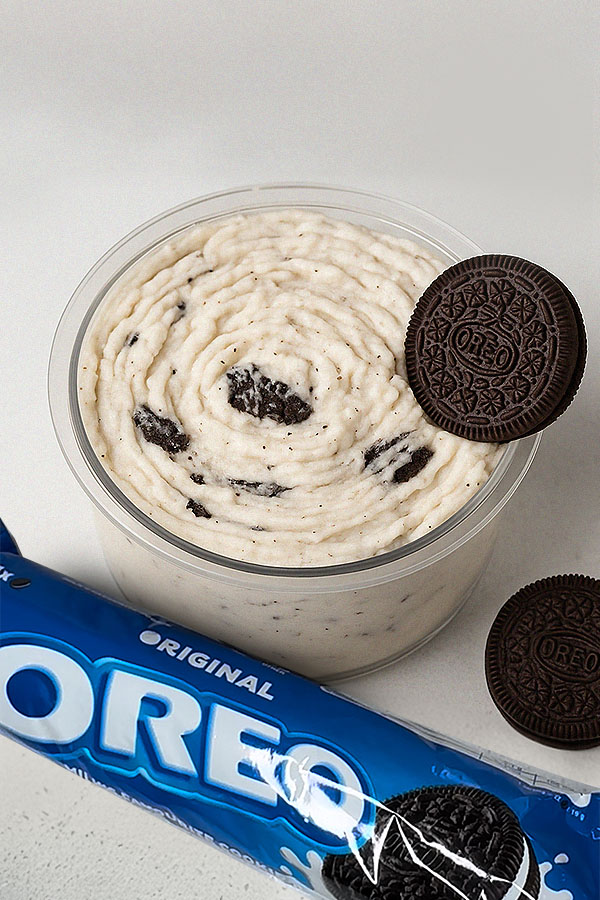 Oreo Ninja Creami Protein Ice Cream Oreo protein ice cream in a clear tub with cookie chunks, topped with an Oreo and a blue Oreo pack beside it.