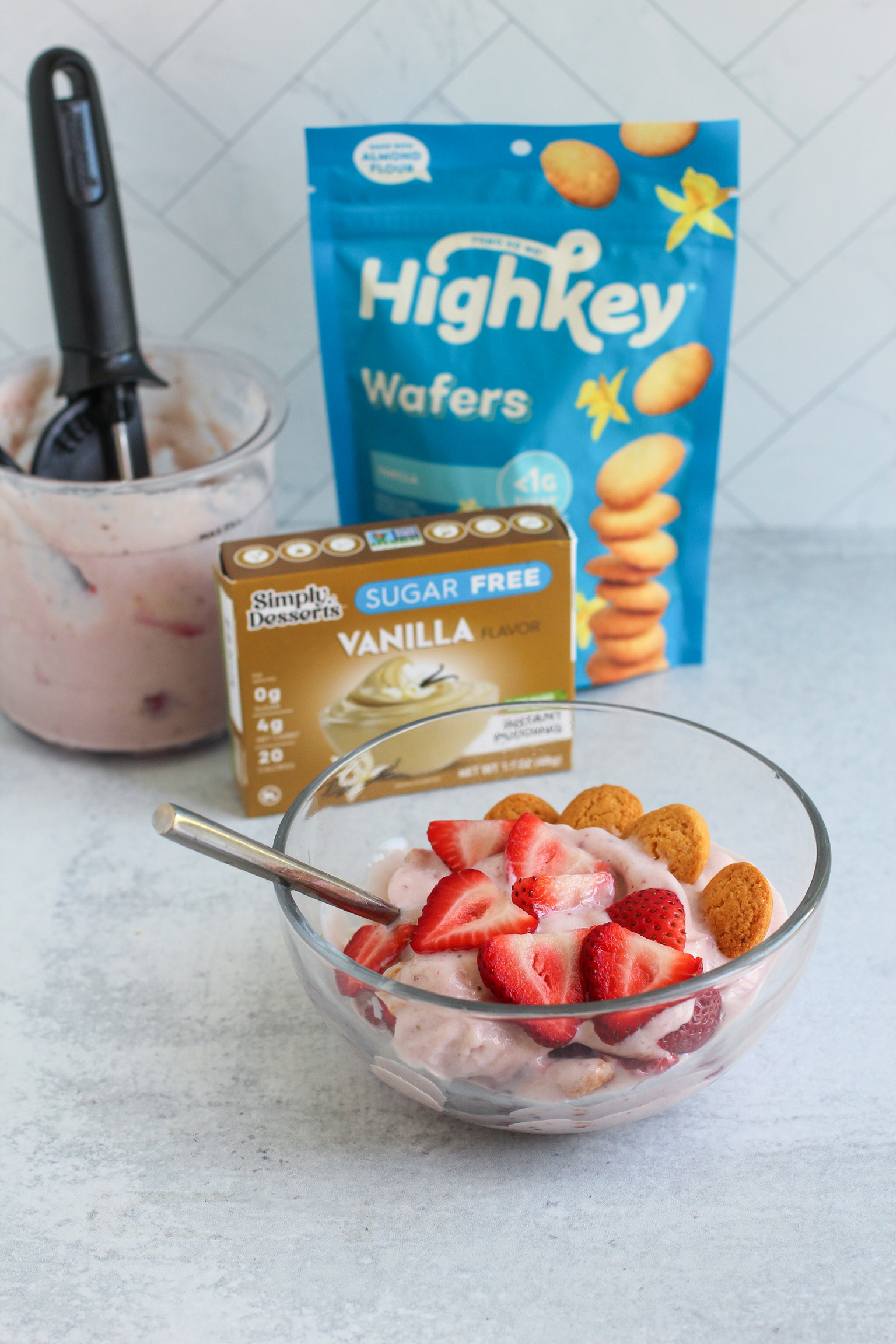 Bowl of strawberry shortcake ice cream with product packaging for Highkey Vanilla Wafers and Simply Delish Vanilla Pudding in the background